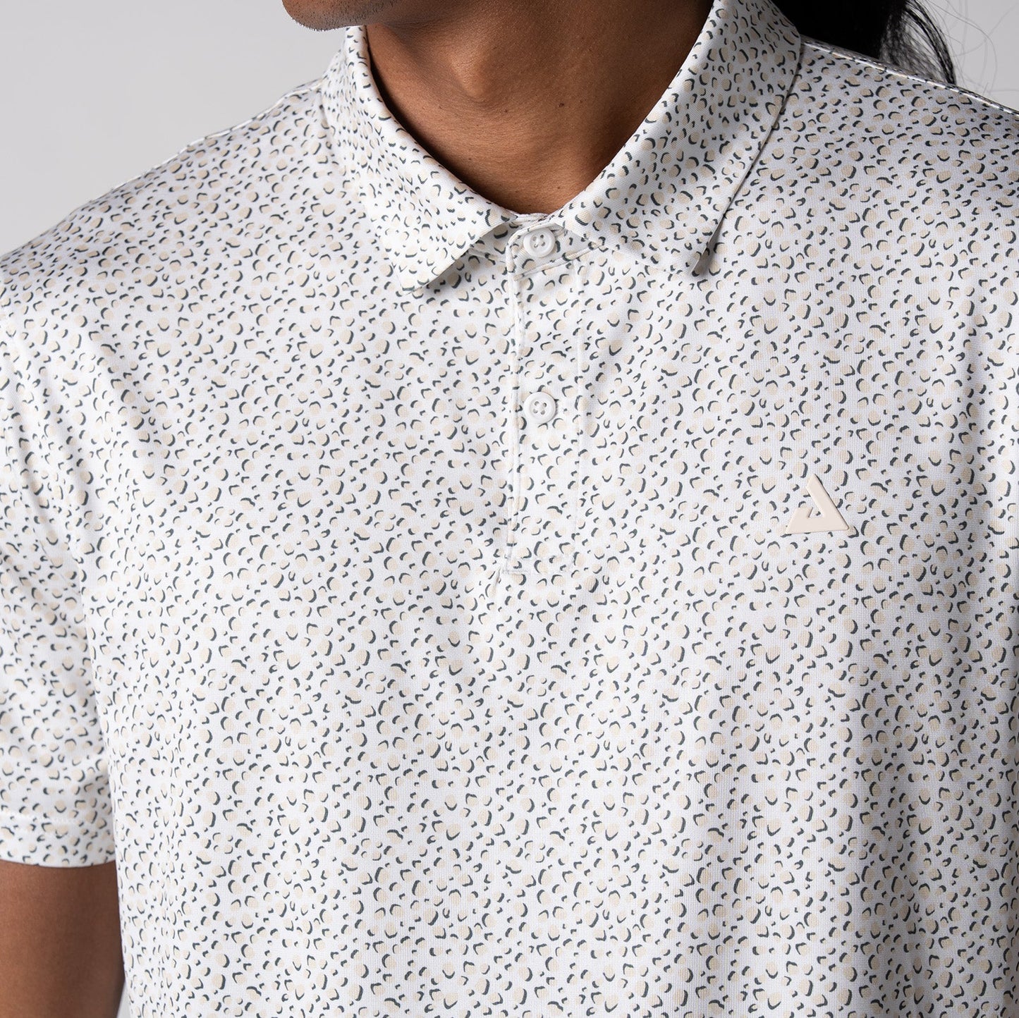 Gray background, close up image of the buttons, collar and raised JOOLA trinity logo on the front of a JOOLA Men's Club Printed Polo, Safari Leopard pattern.