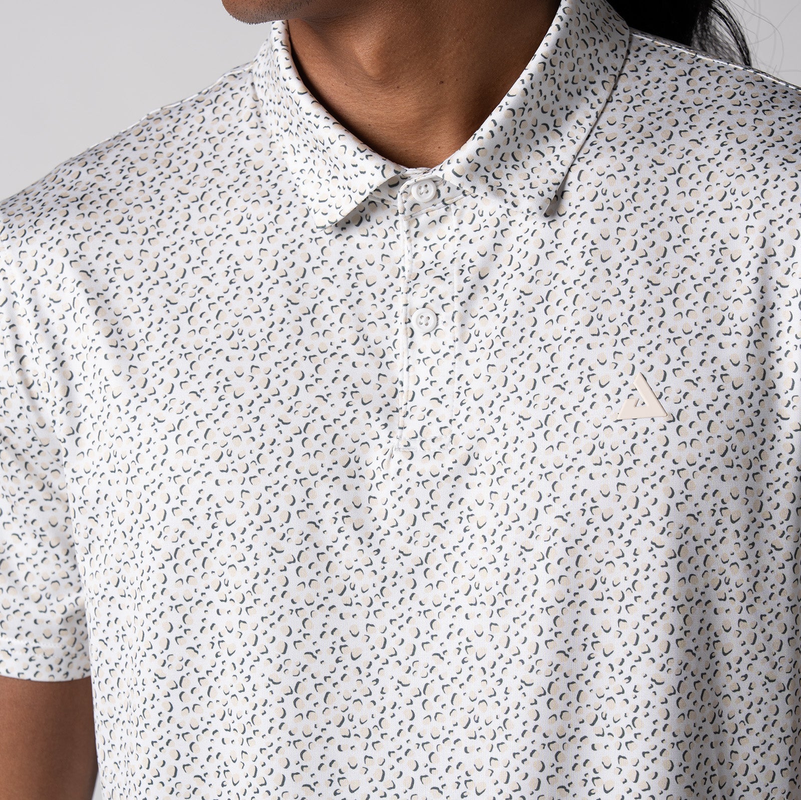 Gray background, close up image of the buttons, collar and raised JOOLA trinity logo on the front of a JOOLA Men's Club Printed Polo, Safari Leopard pattern.