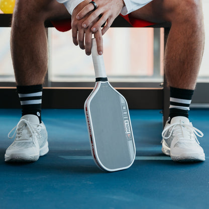 Close up image of the JOOLA Ben Johns Perseus Pro IV Pickleball Paddle in between the shoes of Ben Johns.