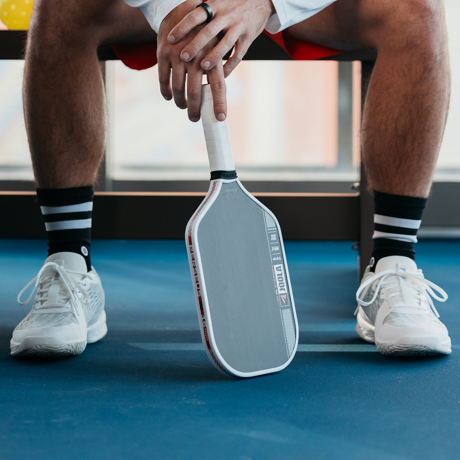 Close up image of the JOOLA Ben Johns Perseus Pro IV Pickleball Paddle in between the shoes of Ben Johns.