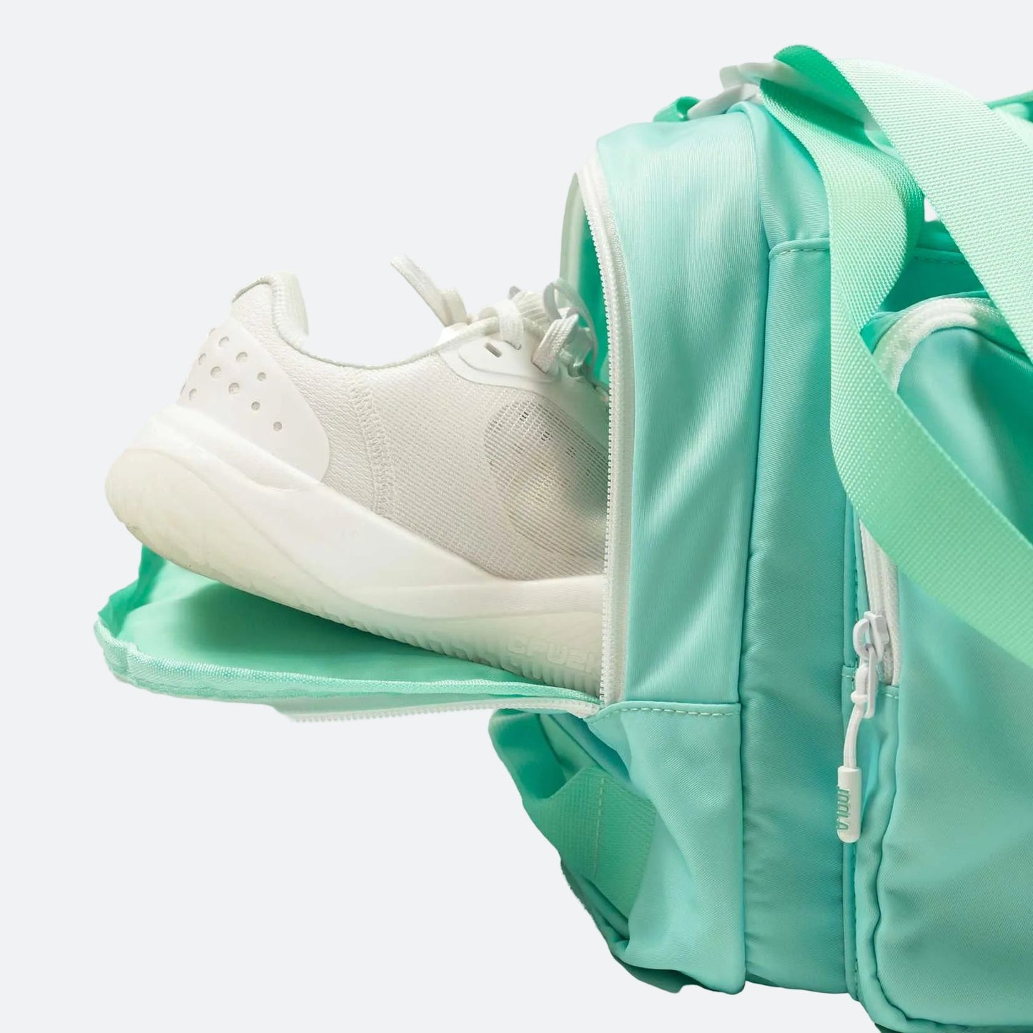 White background, close up image of a pair of shoes in the shoe compartment of the JOOLA duffle bag.