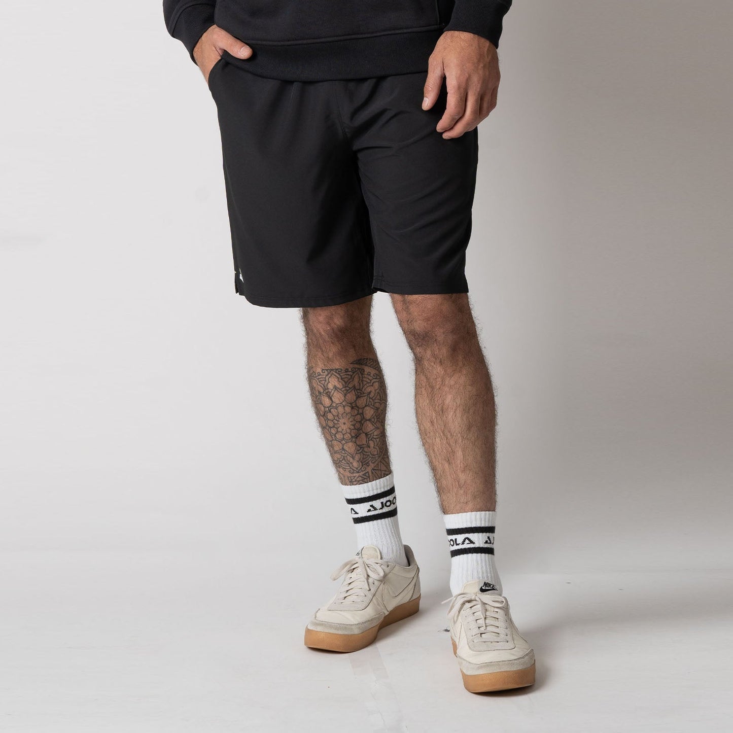 Male model wearing a pair of JOOLA Men's Woven Shorts with a Nine-Inch inseam, black.