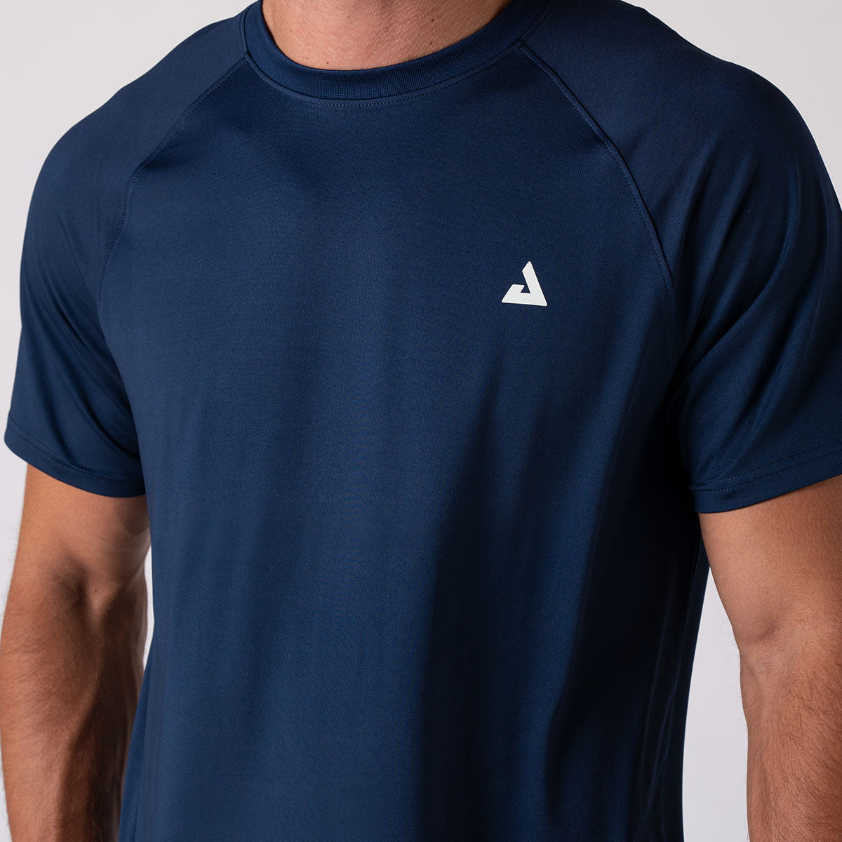 Close up image of the JOOLA Trinity logo above the left breast of a male model wearing a JOOLA Men's Court Short Sleeve, Navy.