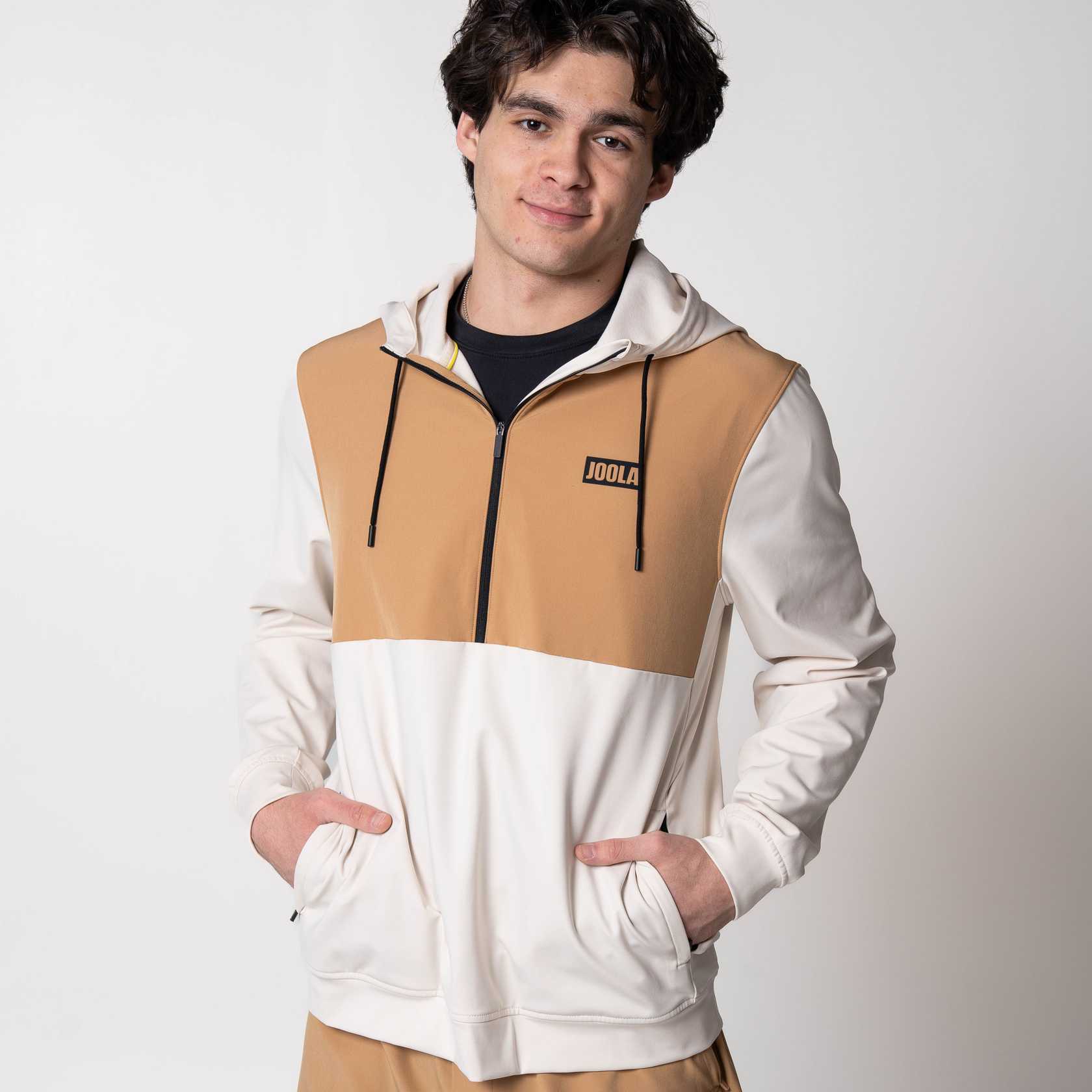 Person wearing a sandstorm and white colored hoodie with JOOLA branding on a plain background.