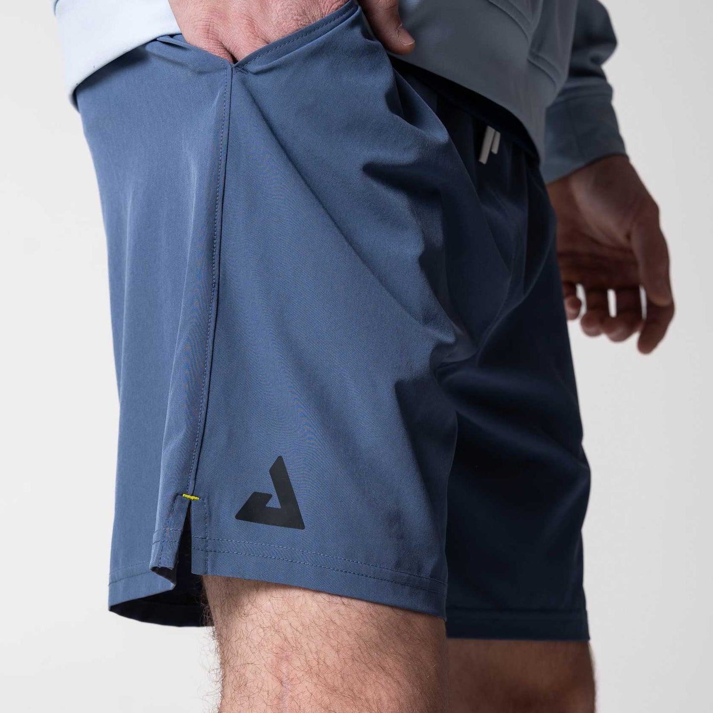 Close-up of the black JOOLA trinity logo on the leg of a pair of JOOLA Woven Shorts, Blue with 7-inch inseam.